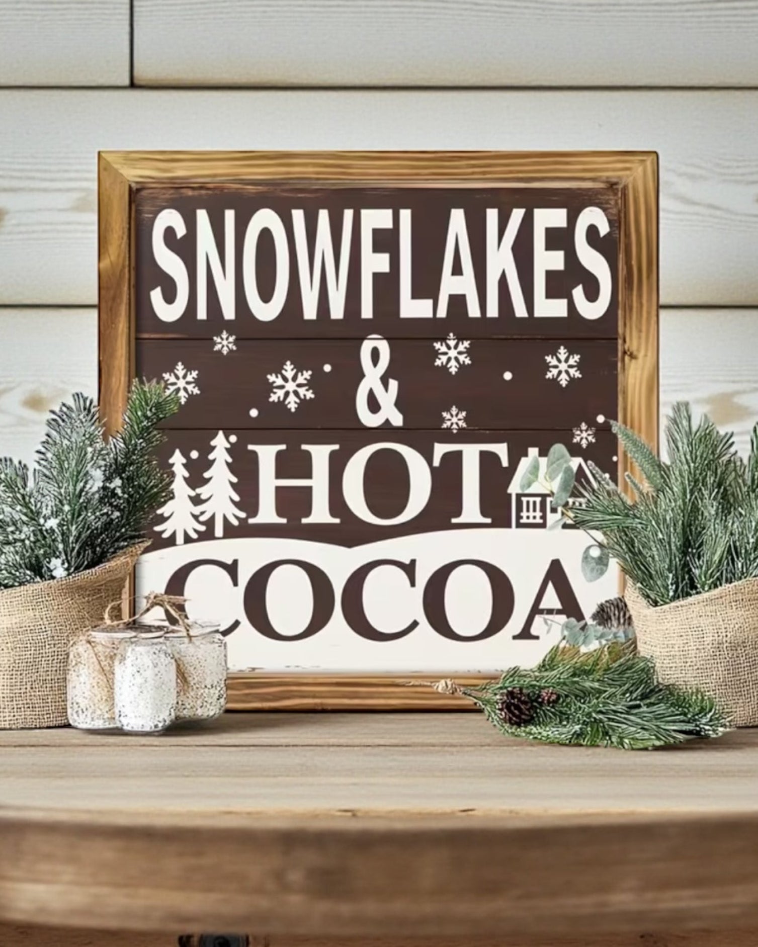 Decorative sign with 'Snowflakes & Hot Cocoa' on a wooden table with festive decor.