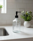 Clear ribbed glass soap dispenser bottle labeled 