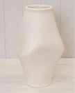 White ribbed vase on a white surface with a light gray background
