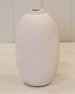 White textured vase on a light wooden surface with a white wooden panel background