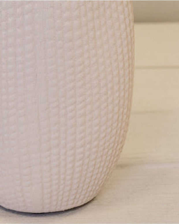White textured vase on a light wooden surface with a white wooden panel background