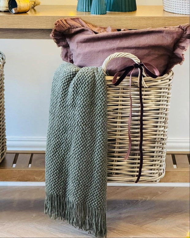 Wicker basket with green textured blanket and brown fabric on a wooden surface.