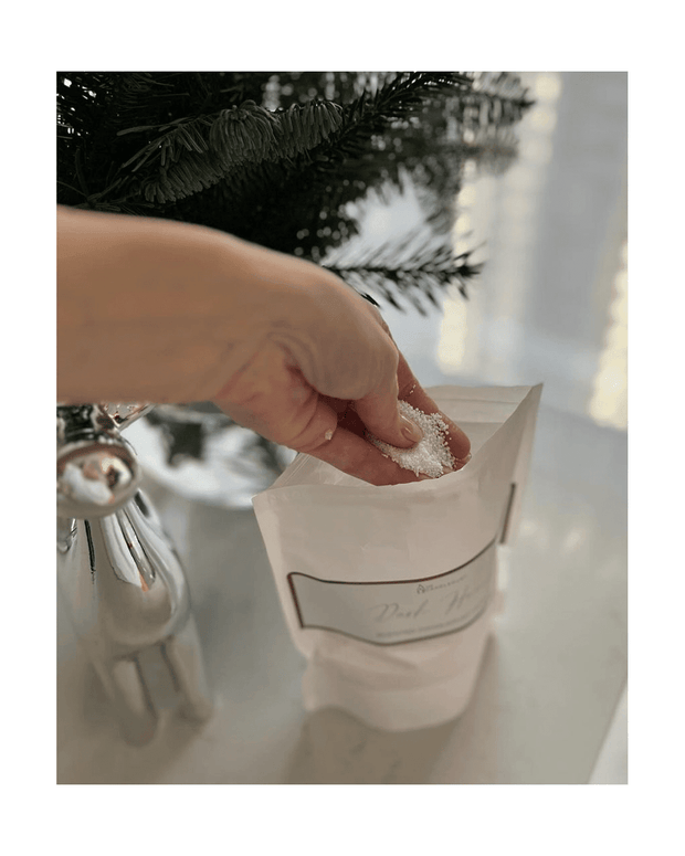 Hand holding a small packet of white powder next to Christmas tree decorations.