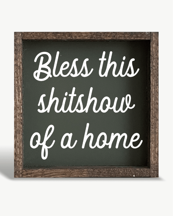Decorative sign with text 'Bless this shitshow of a home' on a white background