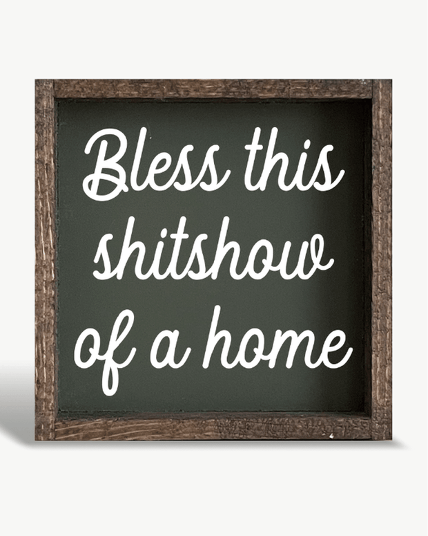 Decorative sign with text 'Bless this shitshow of a home' on a white background