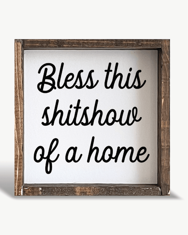 Wooden sign with text 'Bless this shitshow of a home' on a white background
