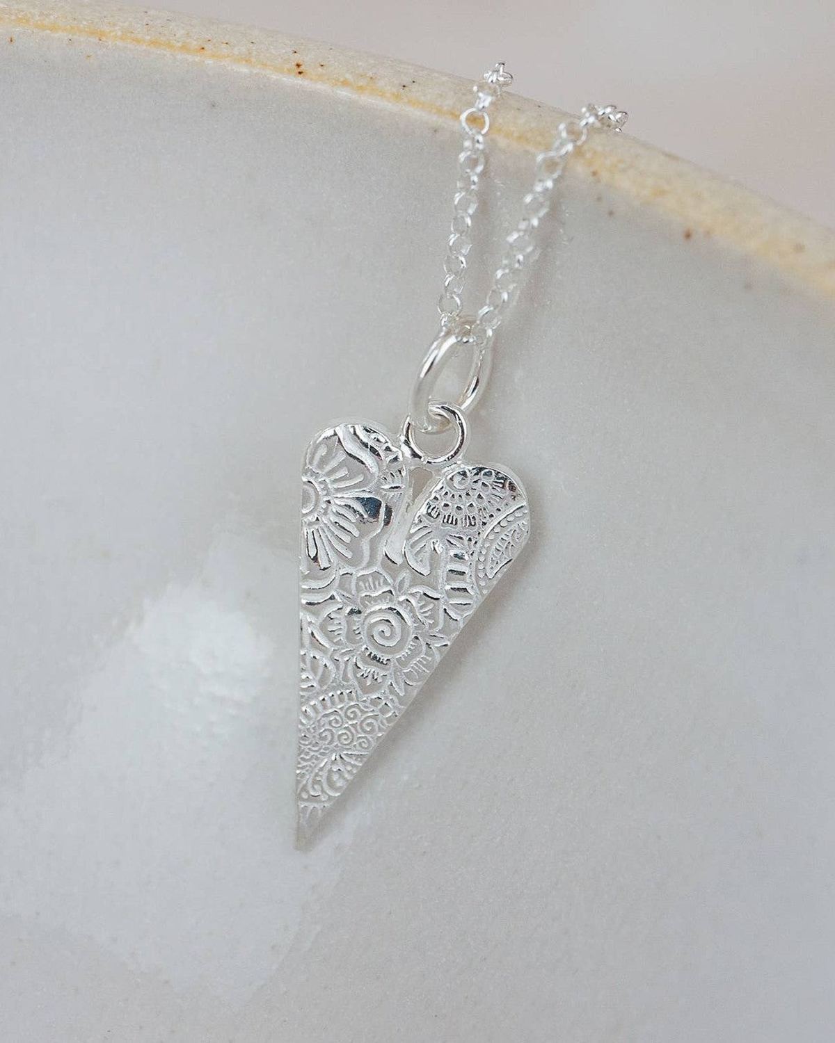 Silver heart-shaped pendant on a chain against a light background
