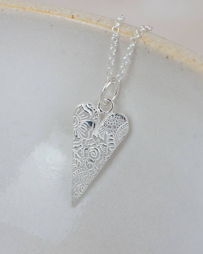Silver heart-shaped pendant on a chain against a light background