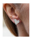 Silver heart-shaped earring worn by a person with a blurred background