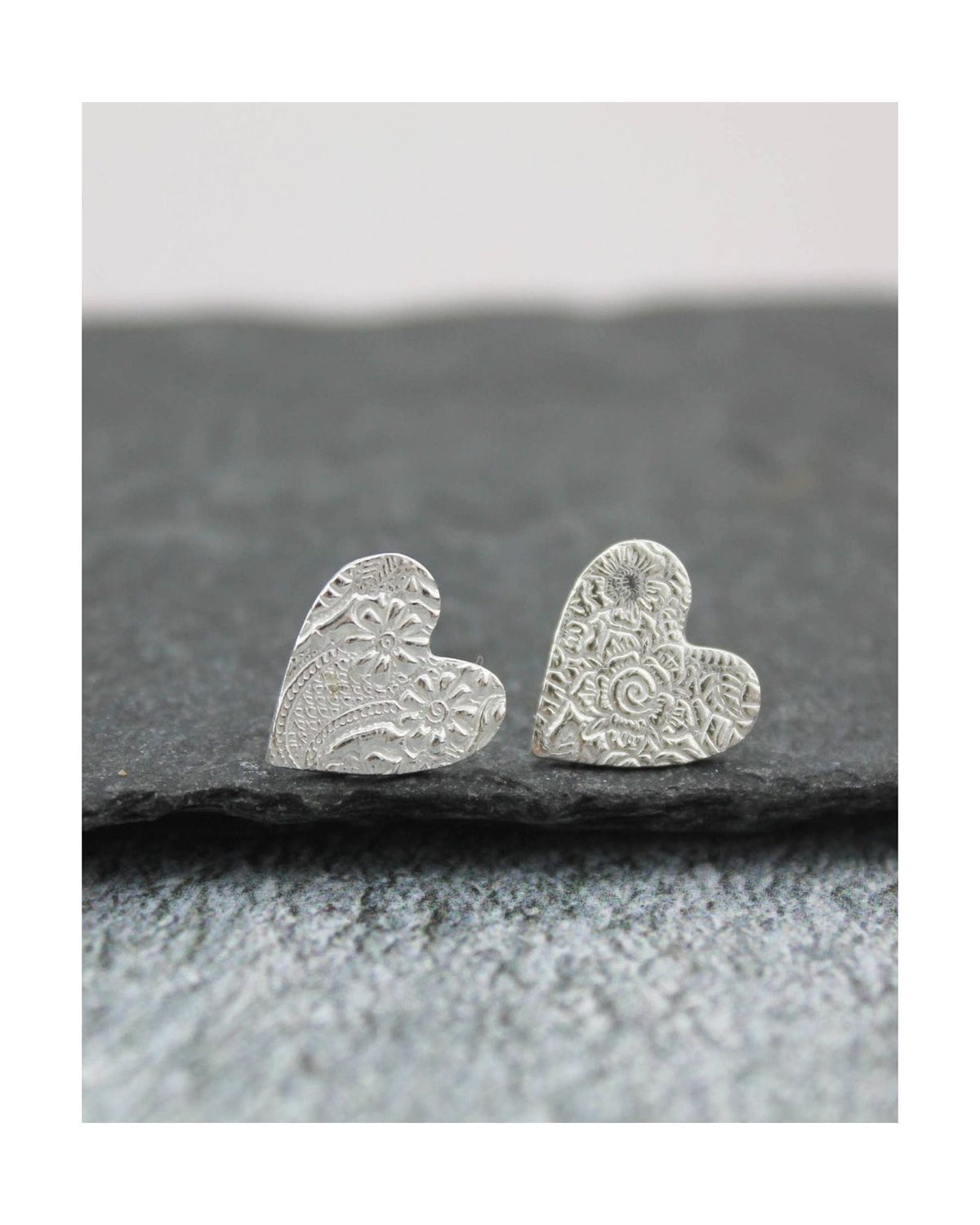 Silver heart-shaped earrings on a dark stone surface