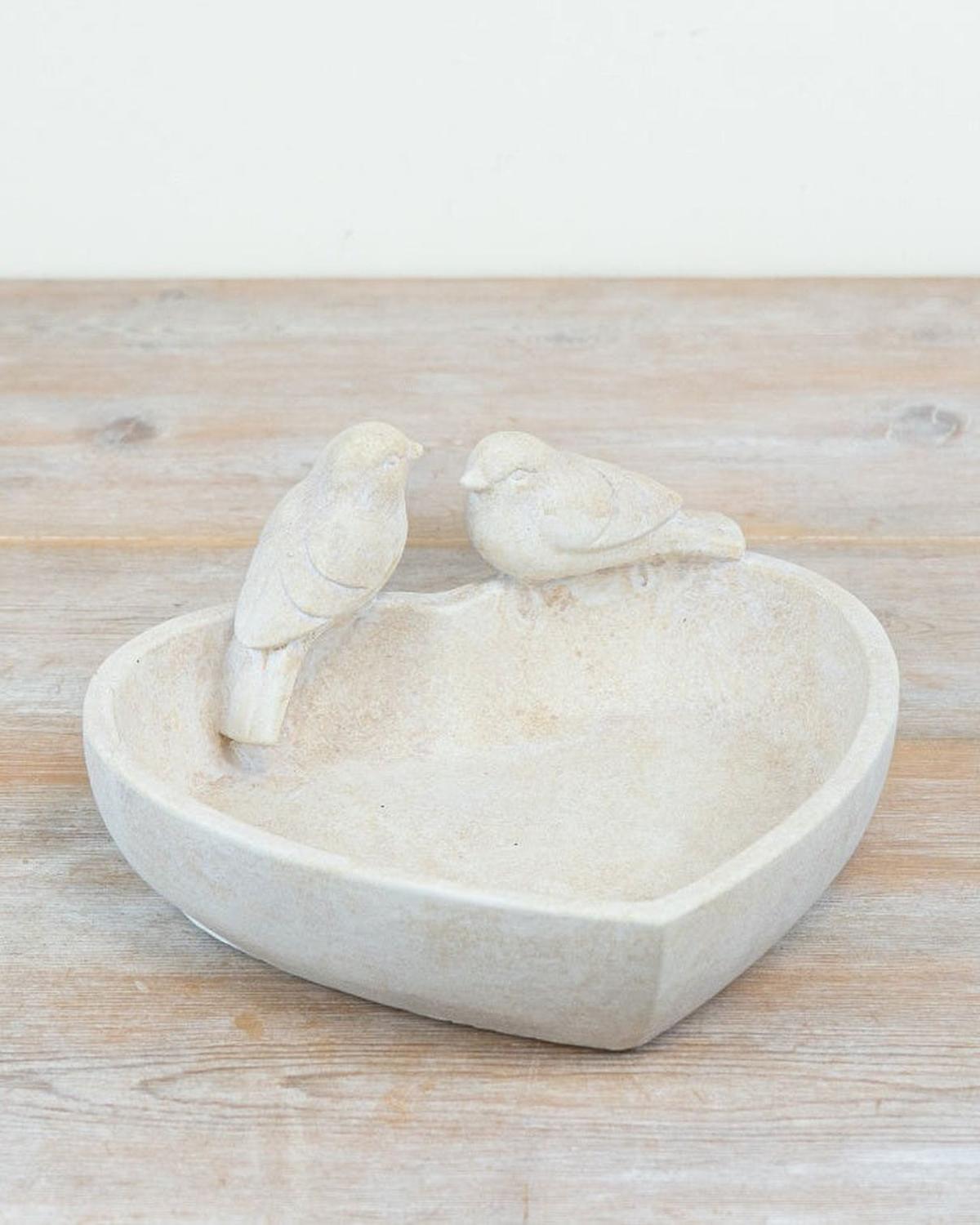 Two white ceramic birds on a heart-shaped dish on a wooden surface