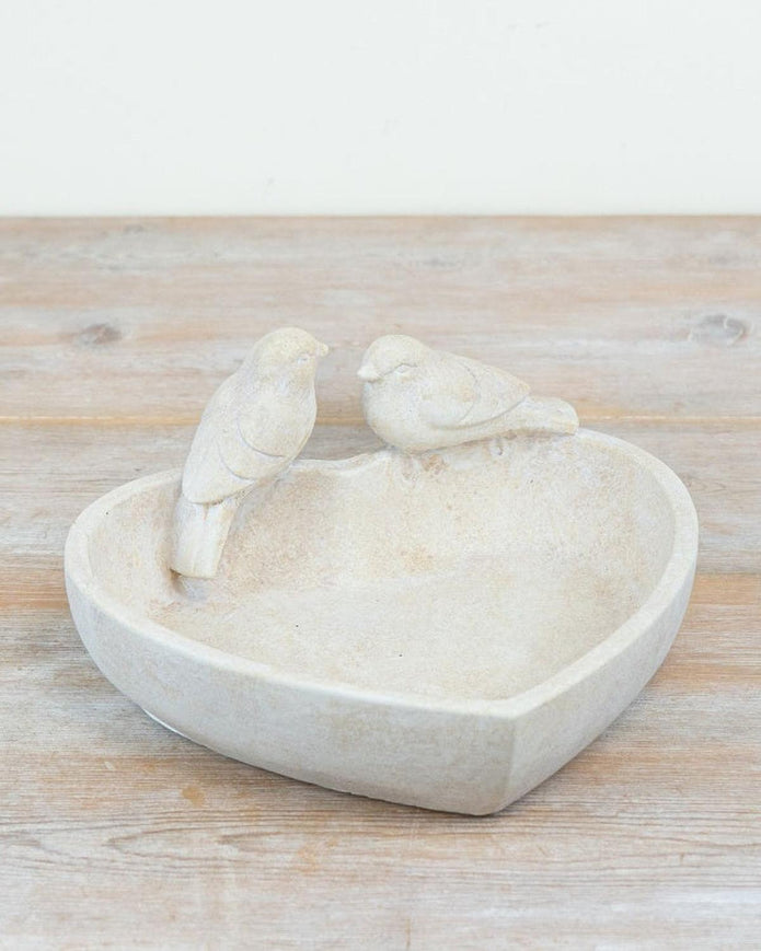 Two white ceramic birds on a heart-shaped dish on a wooden surface
