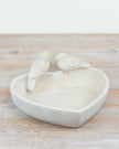 Two white ceramic birds on a heart-shaped dish on a wooden surface