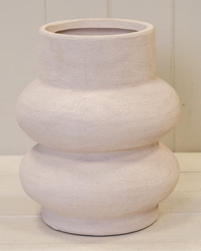 White textured vase on a light wooden surface with a white paneled background