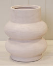 White textured vase on a light wooden surface with a white paneled background