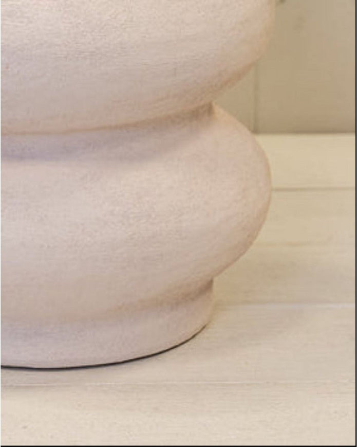 White textured vase on a light wooden surface with a white paneled background