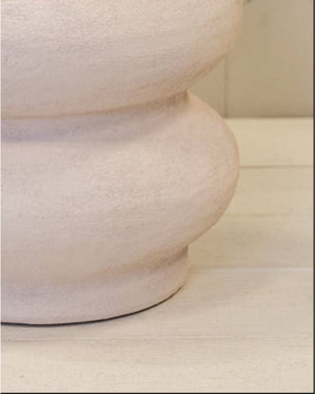 White textured vase on a light wooden surface with a white paneled background