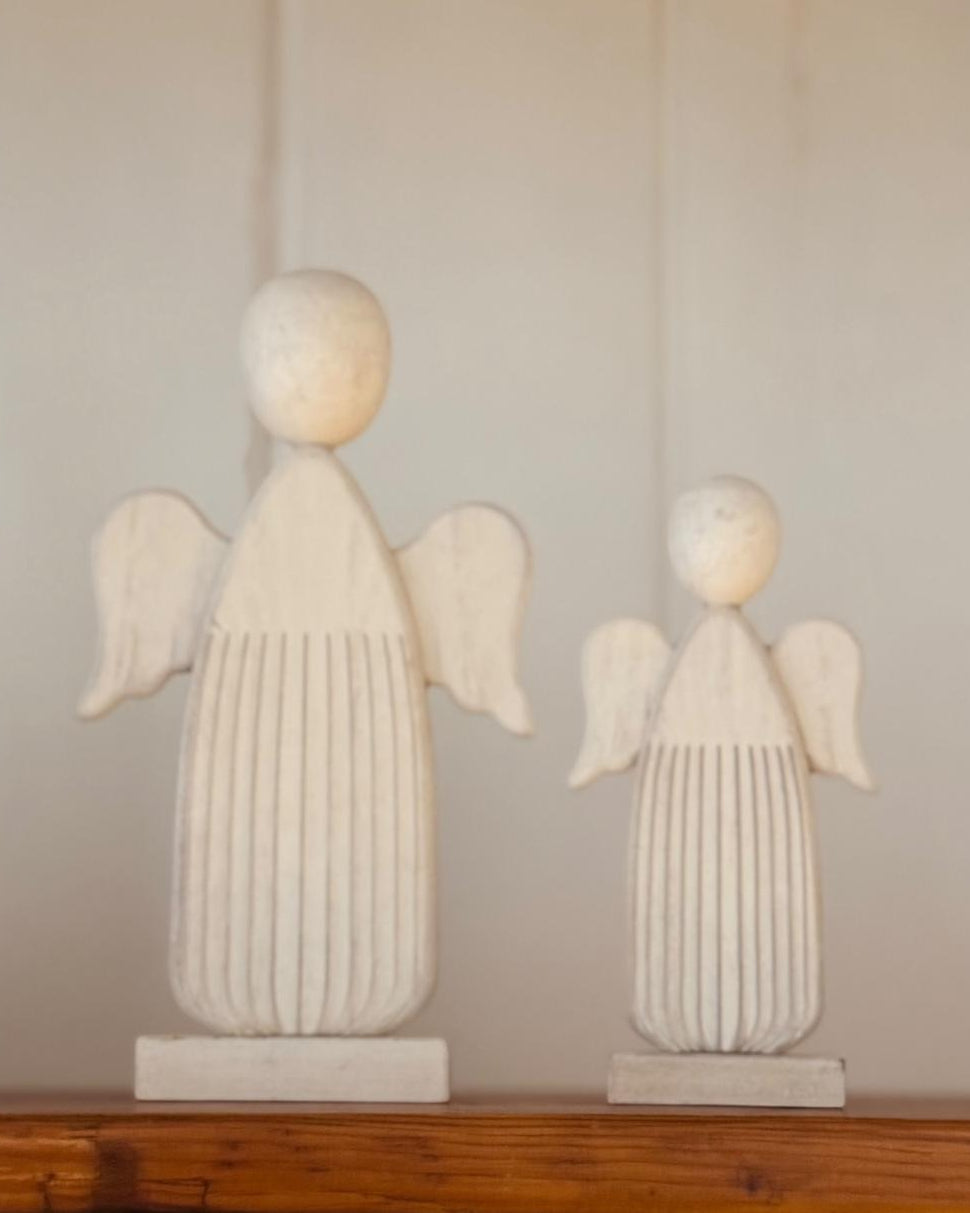 Two white angel statues on a wooden surface with a neutral background