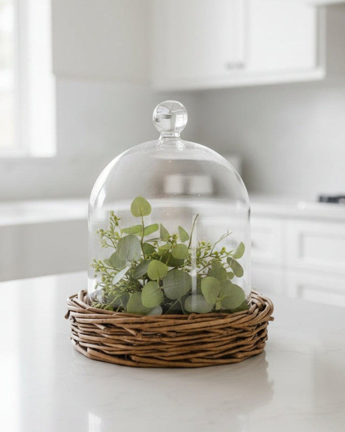 Glass cloche on wicker base, decorative home décor piece by Heaven Sends, showcasing a clear glass dome over a woven wicker stand.