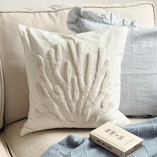 Neutral Embroidered Coral Cushion Cover, cream coral-embroidered cushion beside blue cushions on a sofa
