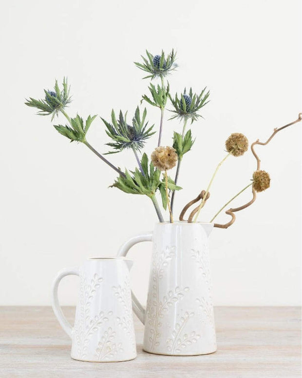 White ceramic pitcher with decorative flowers on a wooden surface