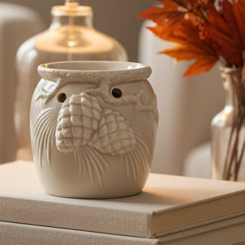 White Christmas Wax Oil Burner With Pinecones, cream pinecone-decorated wax burner beside a vase