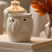 White Christmas Wax Oil Burner With Pinecones, cream pinecone-decorated wax burner beside a vase