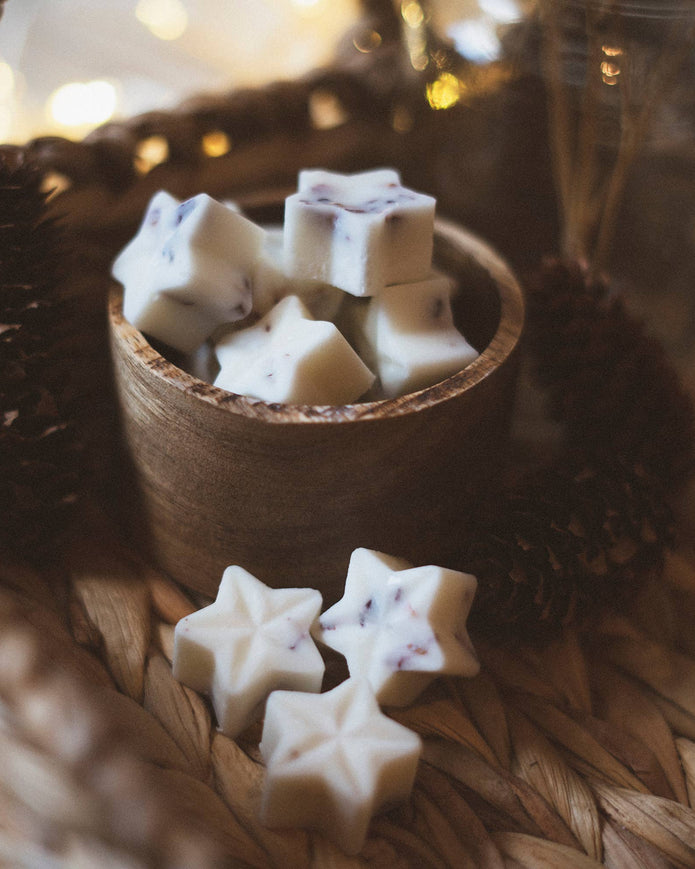 Star-shaped cookies in a wooden bowl on a woven surface with blurred lights in the background