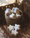 Star-shaped cookies in a wooden bowl on a woven surface with blurred lights in the background