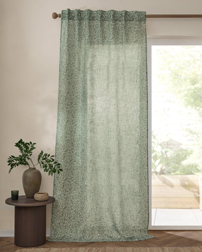 Green curtain with a subtle pattern in front of a window with a view of greenery.