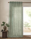 Green curtain with a subtle pattern in front of a window with a view of greenery.
