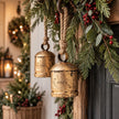Antique gold hanging cow bells styled among pine foliage and red berries, sold individually
