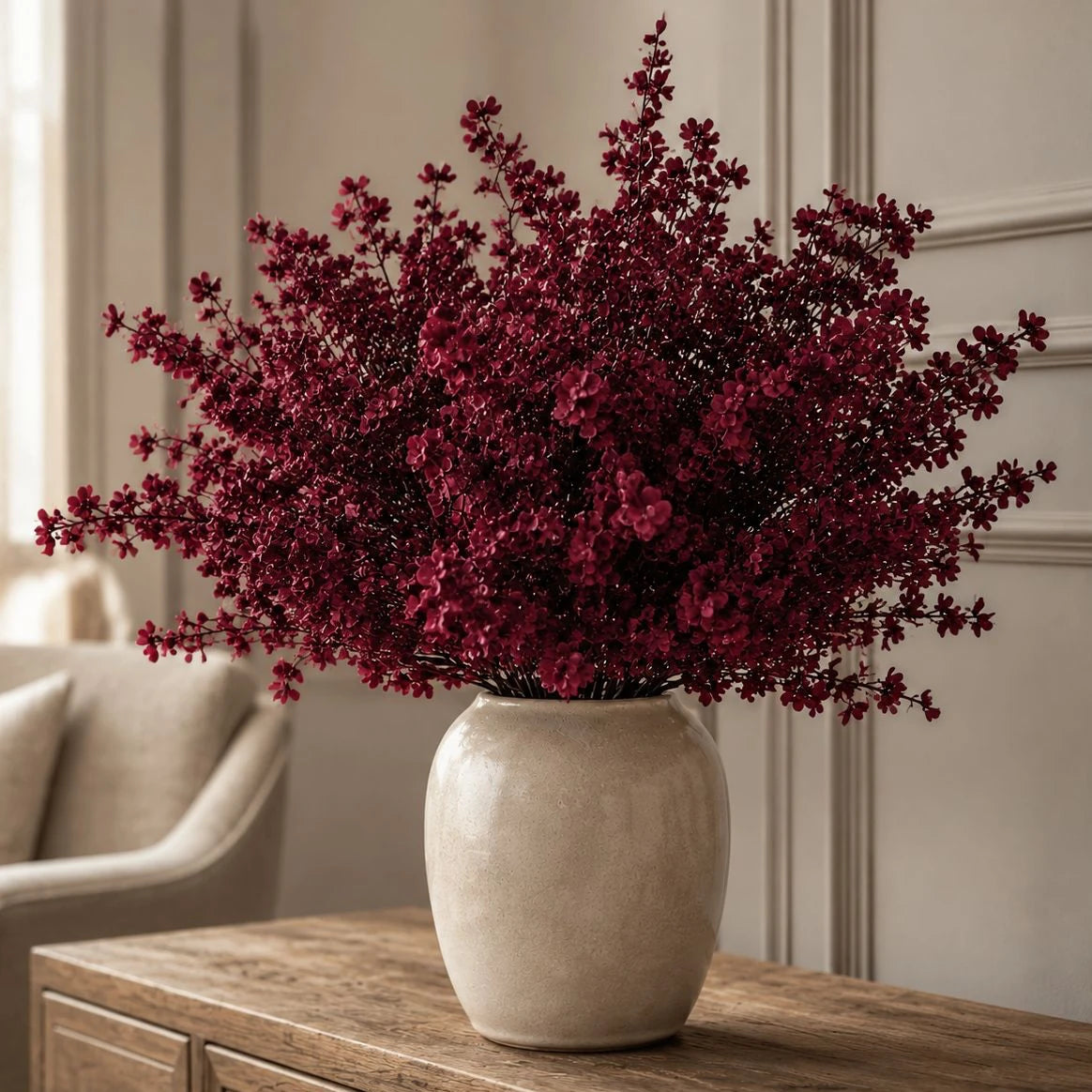 Full burgundy gypsophila arrangement in a neutral ceramic vase on a wooden console.