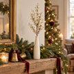 Cream berry stem in a vase on a Christmas mantel with greenery, burgundy ribbon and brass bells.