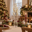 Cream artificial berry stem in a clear vase on a Christmas table with burgundy candles and evergreen place settings.