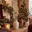 Cream berry stem in a ceramic vase beside a Christmas garland and softly glowing tree.