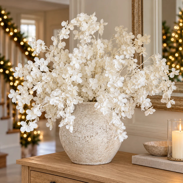 Full arrangement of multiple artificial white blossom stems in a neutral stone vase; vase not included.