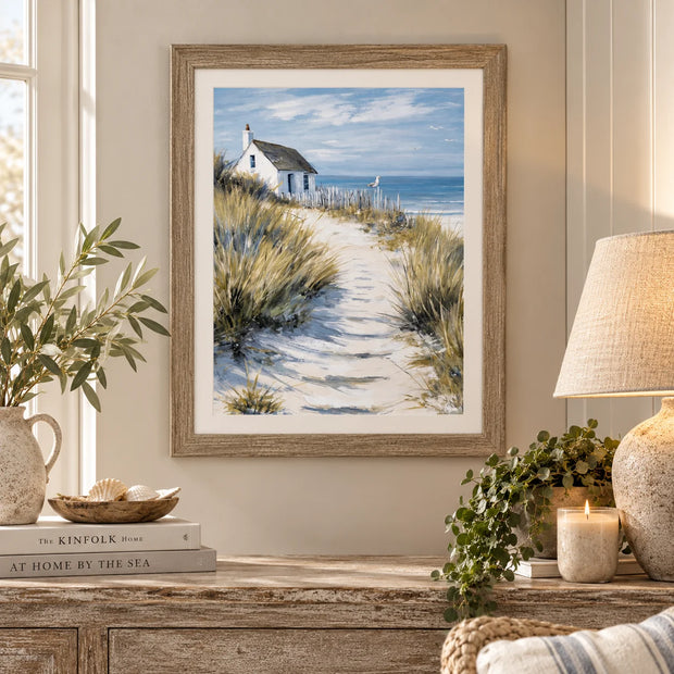 Dune Cottage coastal framed artwork styled above a wooden sideboard with neutral pottery and a table lamp
