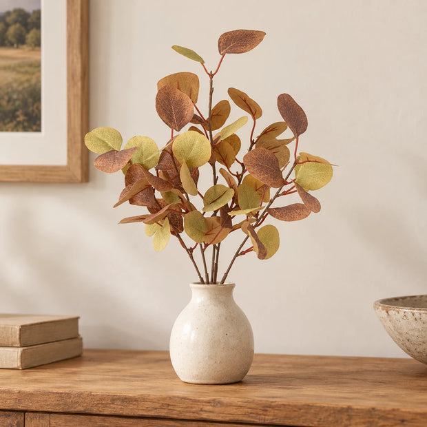 Autumn eucalyptus sprig in a cream vase on an oak console.