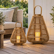 Two bamboo LED candle lanterns on a wooden veranda beside a woven sofa
