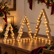 Beige wooden LED tree set glowing on a dark oak Christmas sideboard