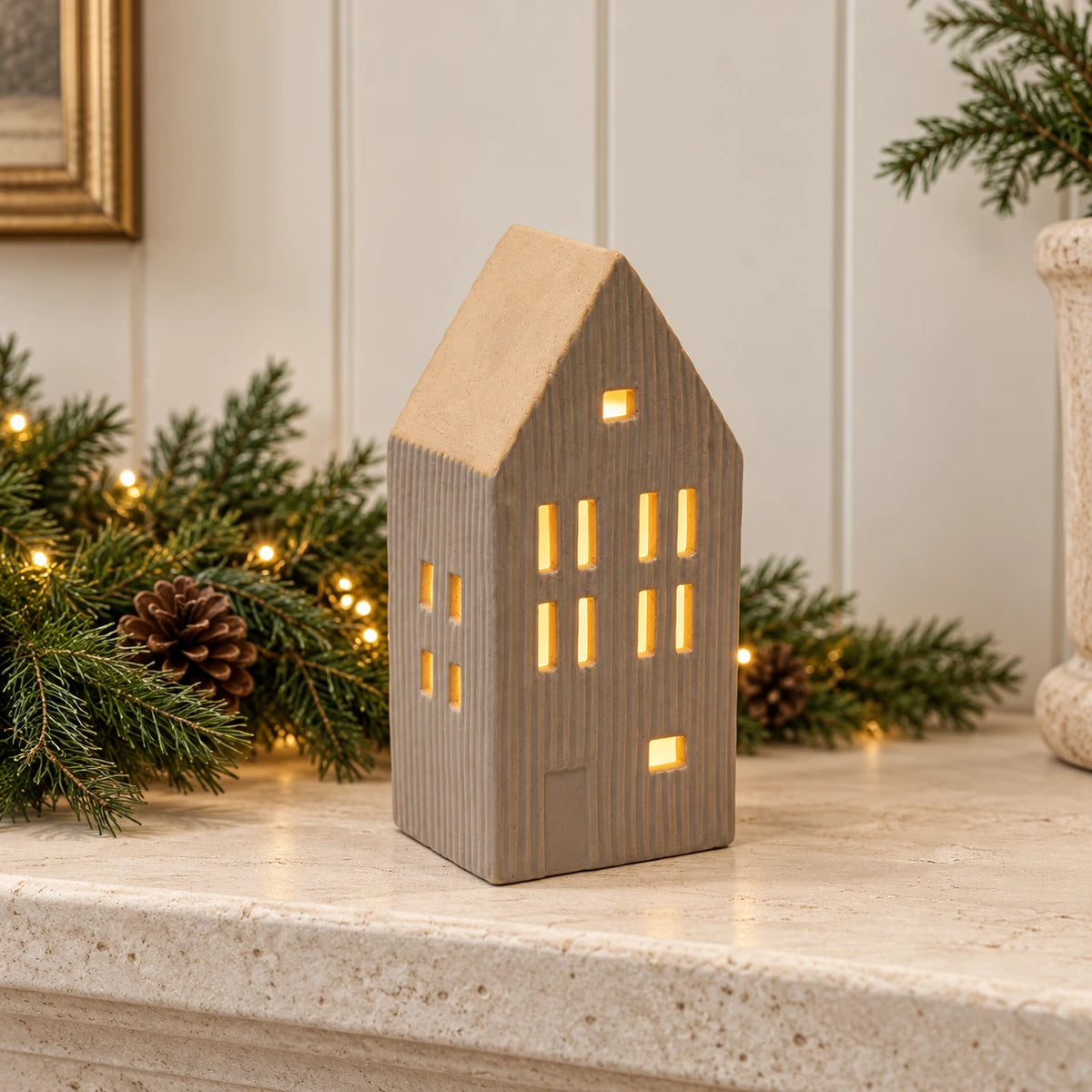 Beige ceramic LED house styled on a limestone mantel with Christmas greenery