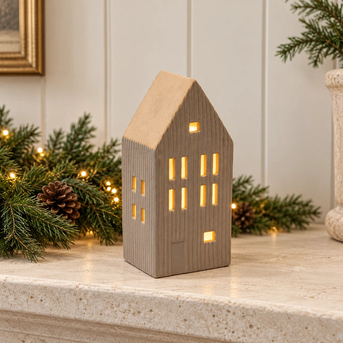 Beige ceramic LED house styled on a limestone mantel with Christmas greenery