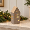Beige ceramic LED house styled on a limestone mantel with Christmas greenery