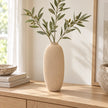 Beige textured stone vase with faux olive stems on a light oak console