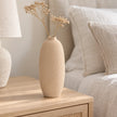 Beige textured stone vase with dried stems on an oak bedside table