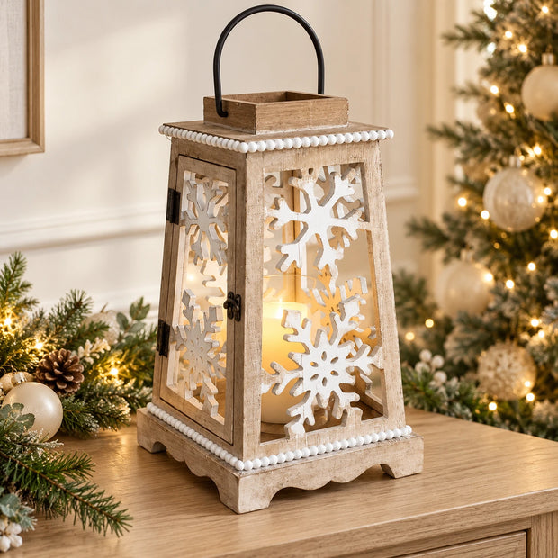 Beige wooden snowflake lantern glowing beside a Christmas tree on an oak console