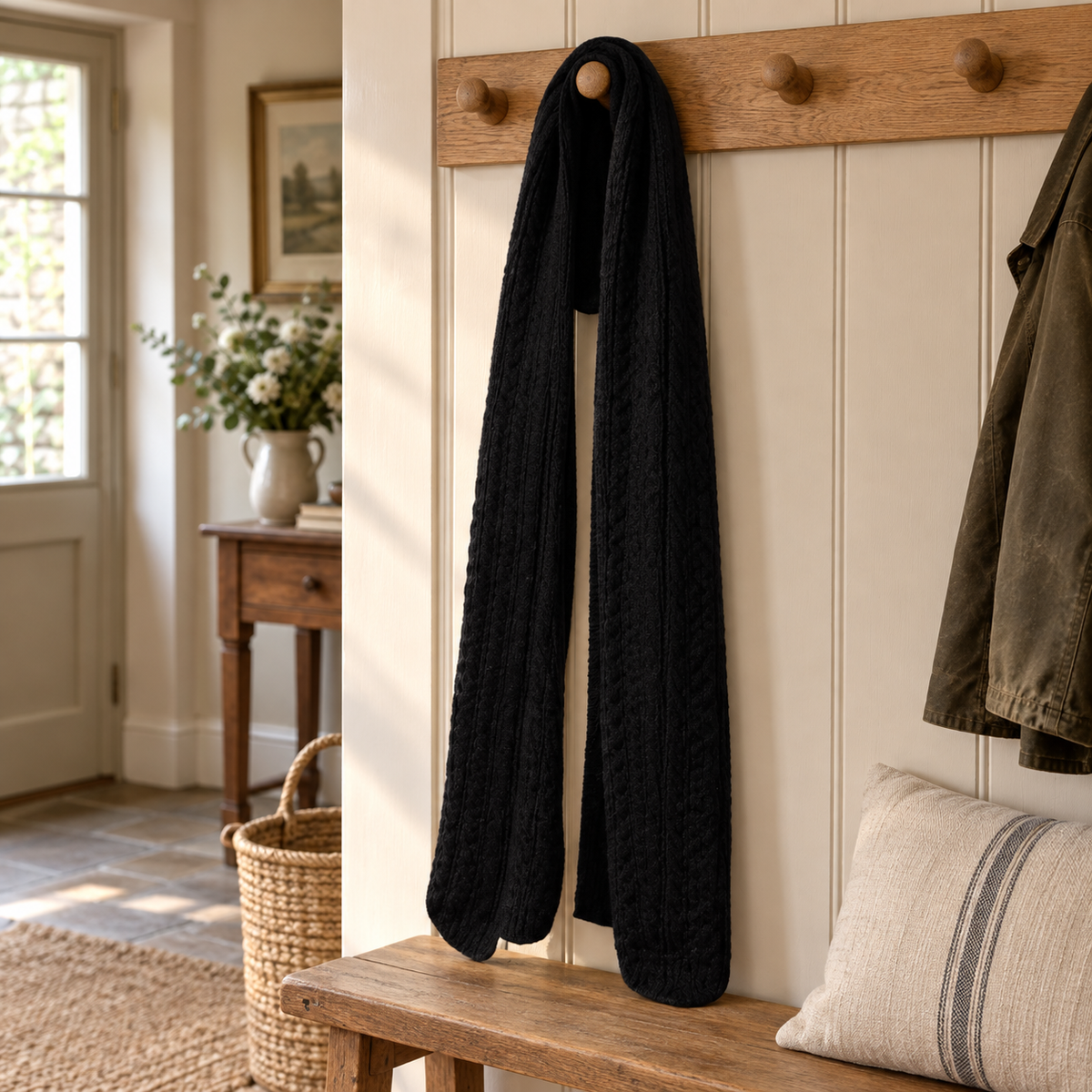 Black cable knit scarf hanging on an oak peg rail in a country hallway