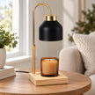 Black enamel effect candle warmer on a wooden side table beside a window with an unlit candle