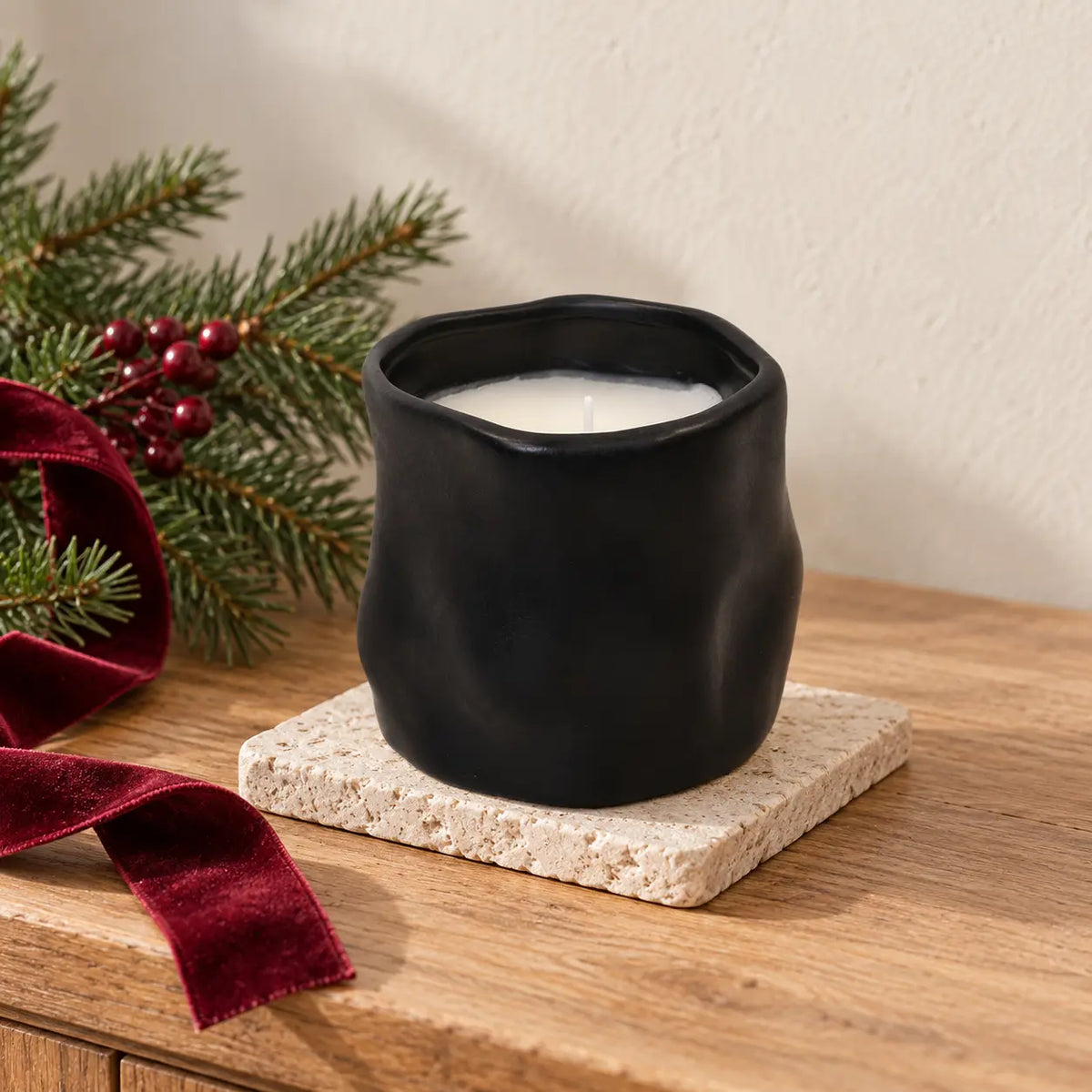 Unlit black sculpted vessel candle beside Christmas greenery and burgundy ribbon